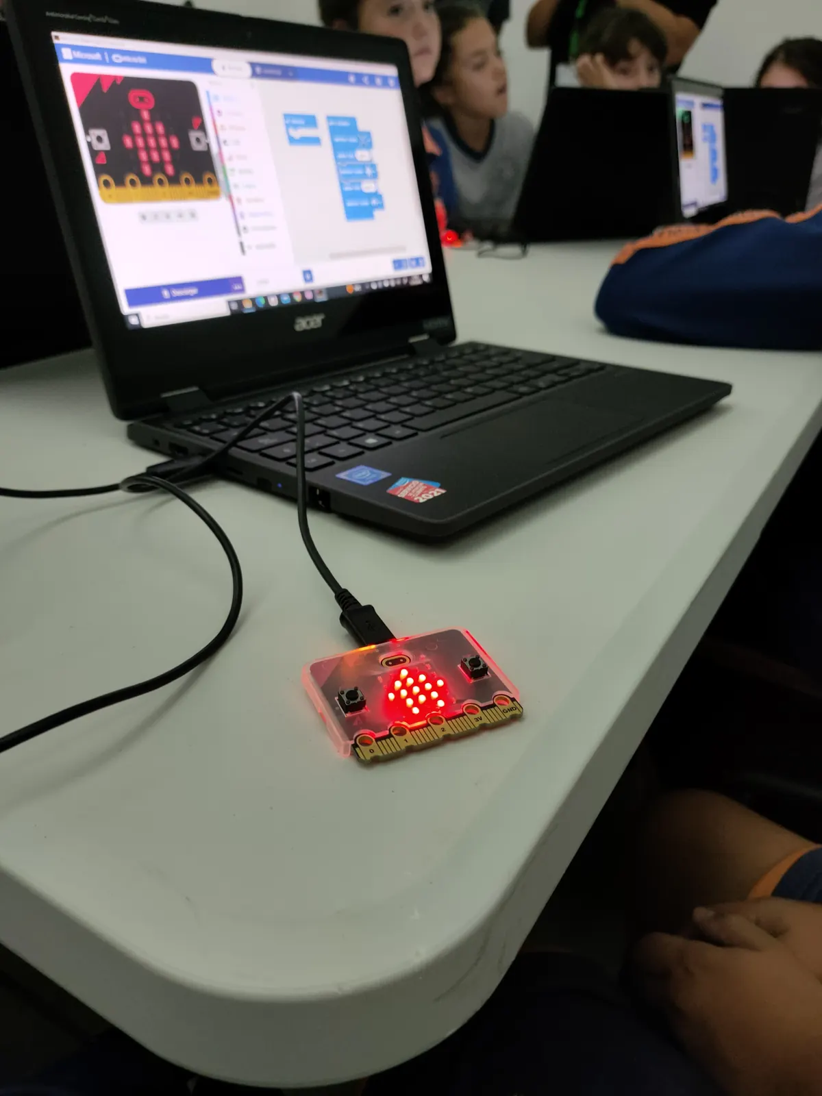 Portátil con un editor de bloques y una placa micro:bit conectada, durante un taller